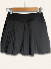 Black pleated skirt on a wooden hanger against a white background