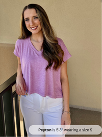 /Mauve/ Woman wearing a purple shirt and white pants standing against a beige wall.