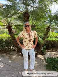 Woman wearing a patterned shirt and white pants standing in front of palm trees.