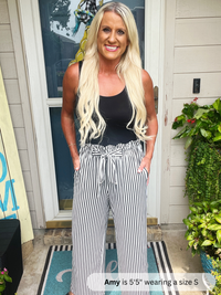 Woman wearing a black tank top and striped pants standing outside a house.