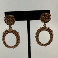 Gold textured dangle earrings with circular studs and larger open oval pendants, both featuring a rough, organic surface, displayed on a black stand against a plain light background.