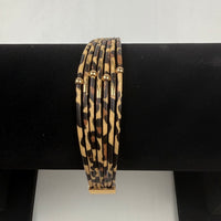 A set of six thin bangle bracelets with a leopard print pattern and small gold accents, displayed on a black bracelet stand.