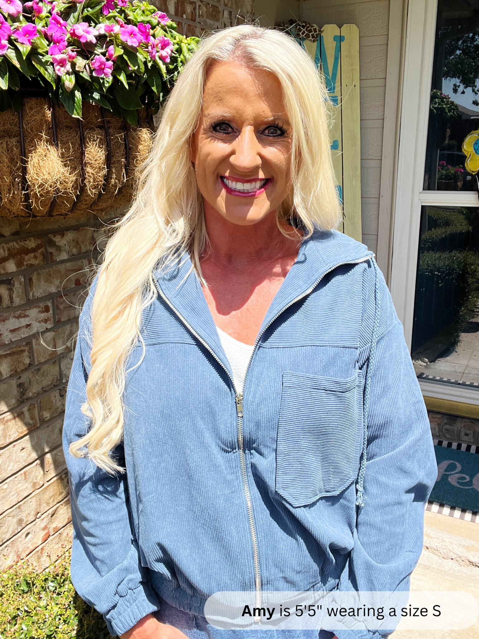 Woman wearing a blue jacket standing outdoors with flowers and a door in the background