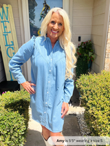 Woman wearing a light blue dress standing outside a house with 'Welcome' sign.