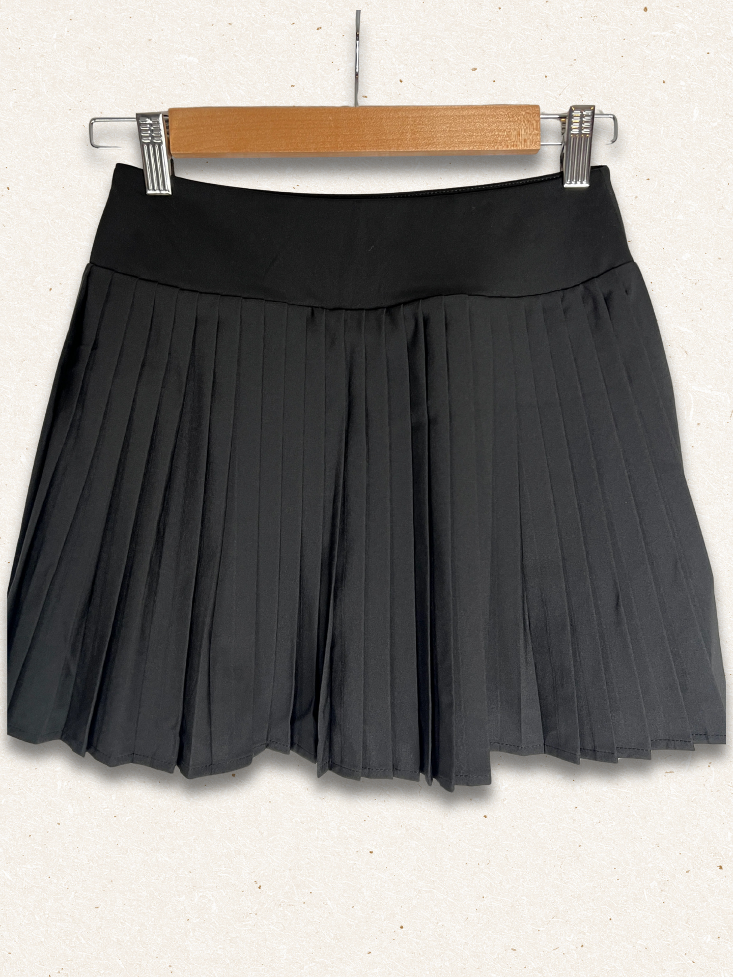Black pleated skirt on a wooden hanger against a white background
