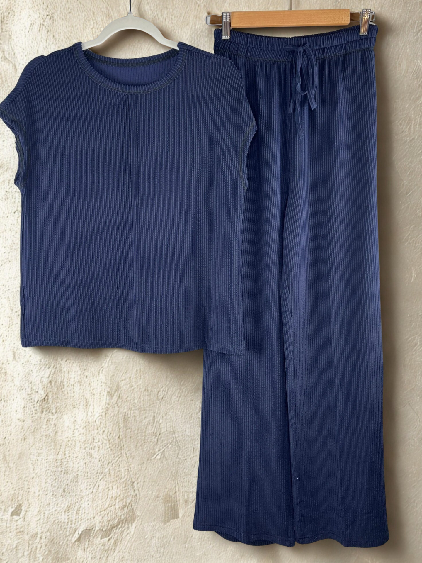 Navy blue ribbed top and pants on hangers against a textured beige wall.