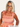 Woman wearing a peach dress with ruffled straps on a plain background