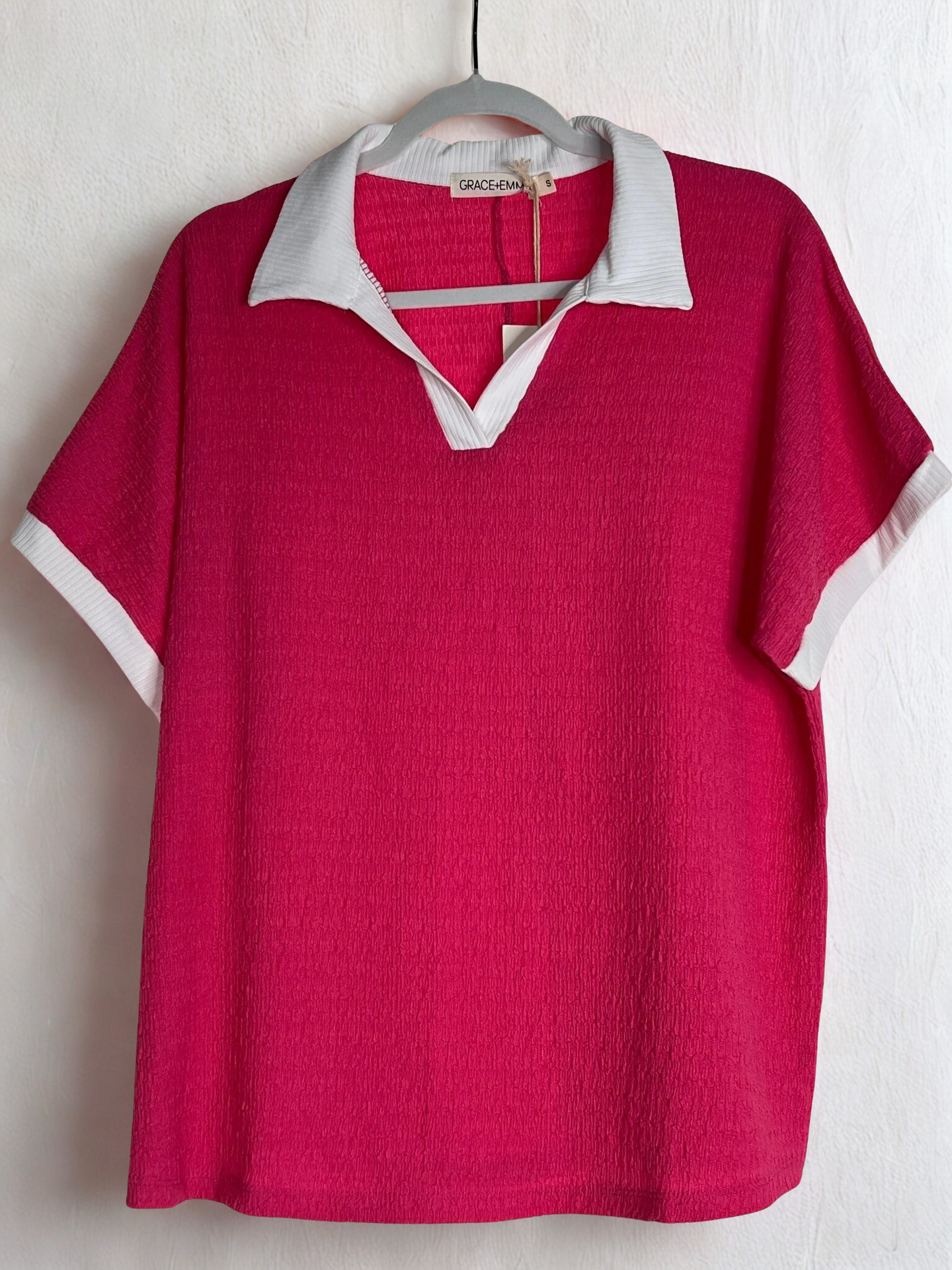 Red polo shirt with white collar and trim on a hanger against a white background