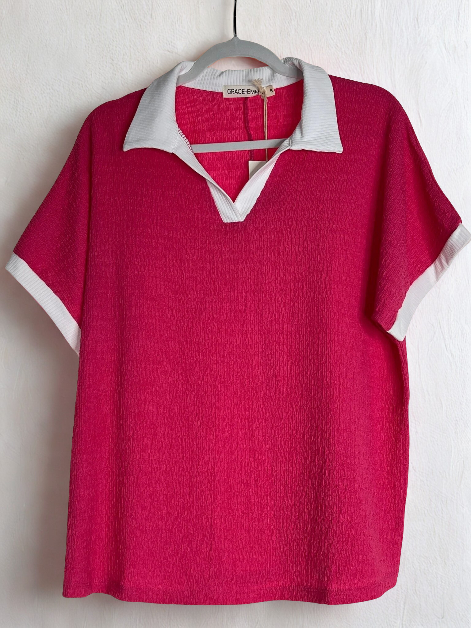 Red polo shirt with white collar and trim on a hanger against a white background