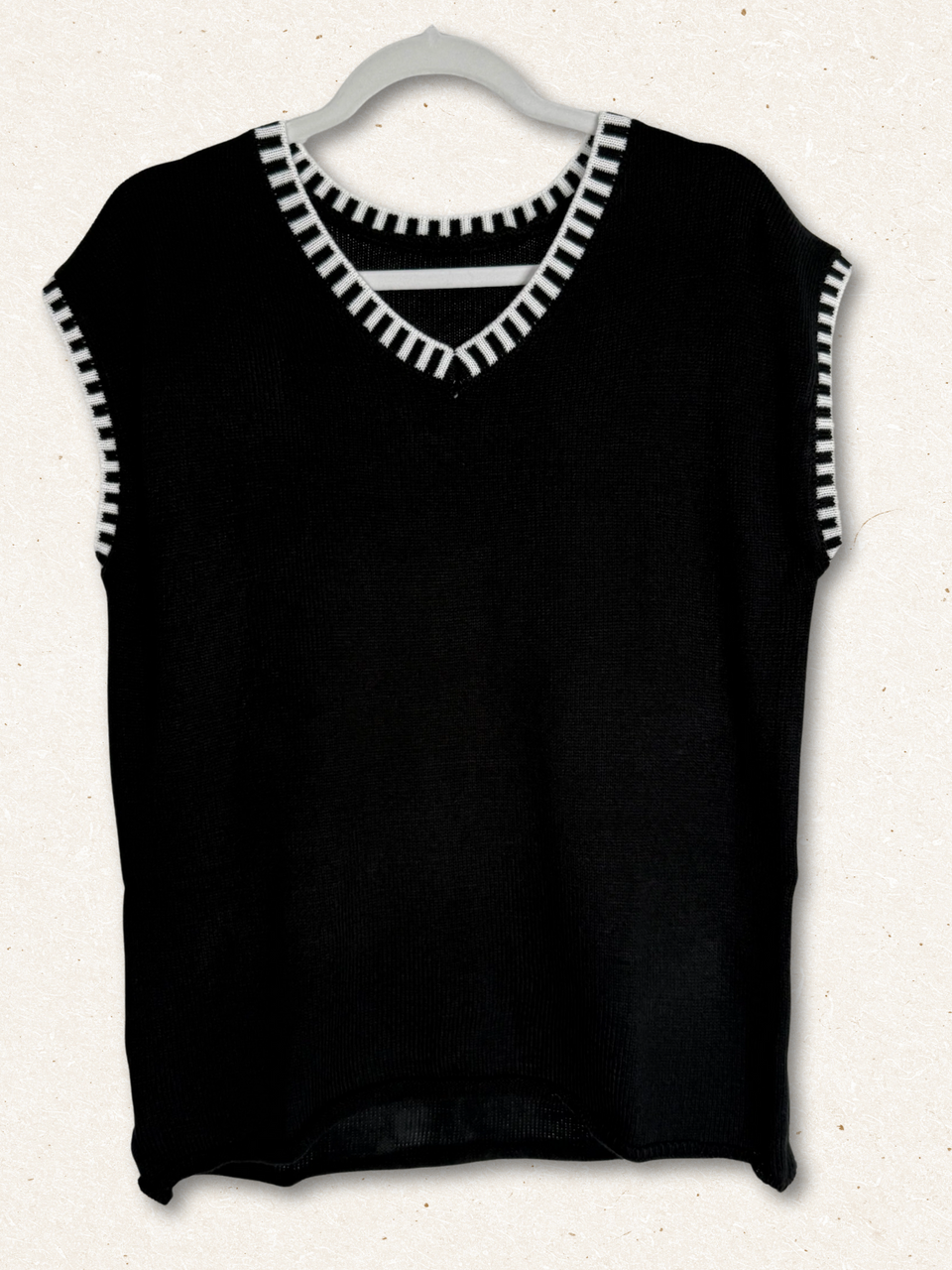 /Black/ Black sleeveless top with white trim on a hanger against a white background