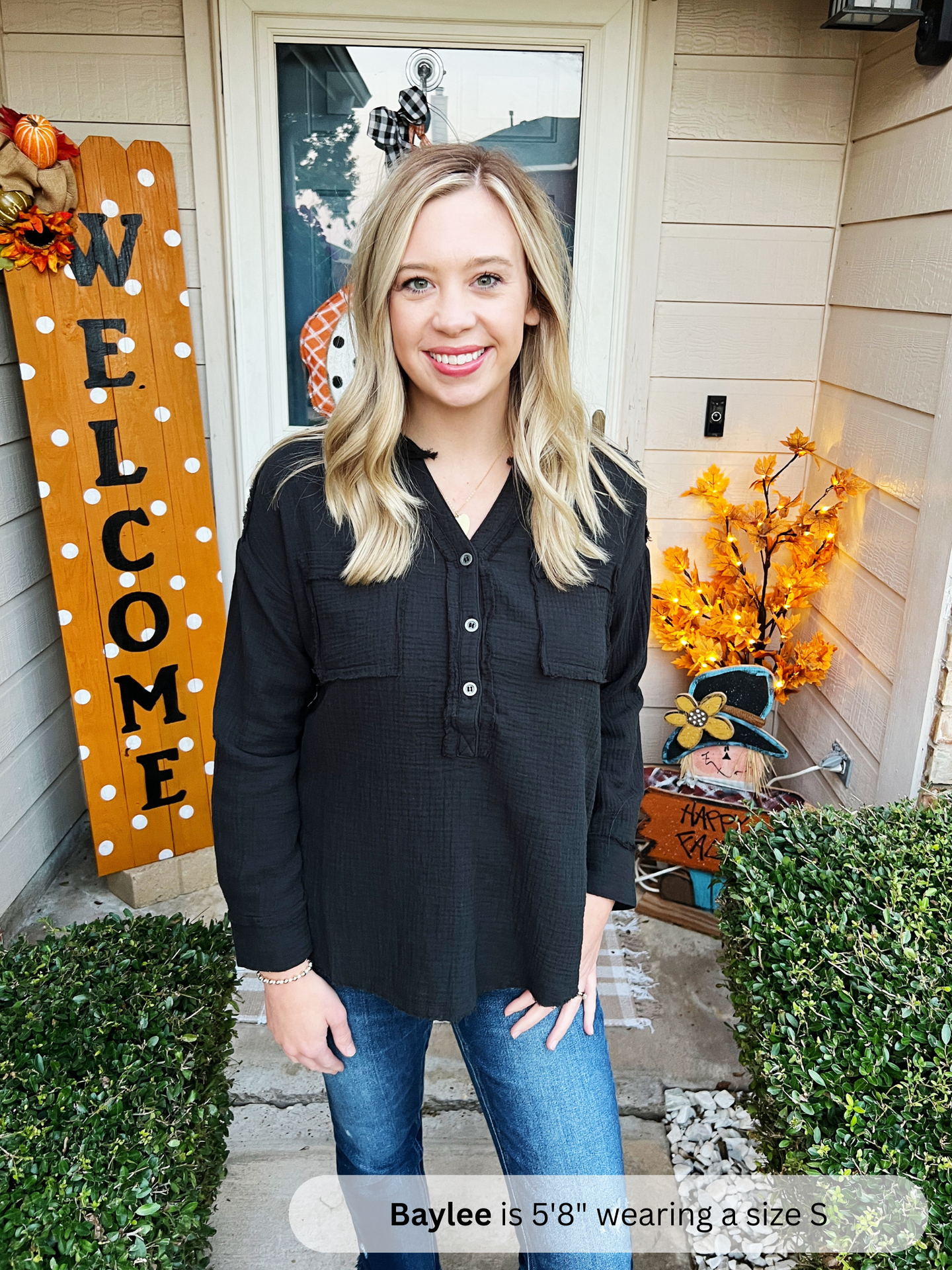 Woman standing in front of a house with Halloween decorations, including a 'Welcome' sign and pumpkins.