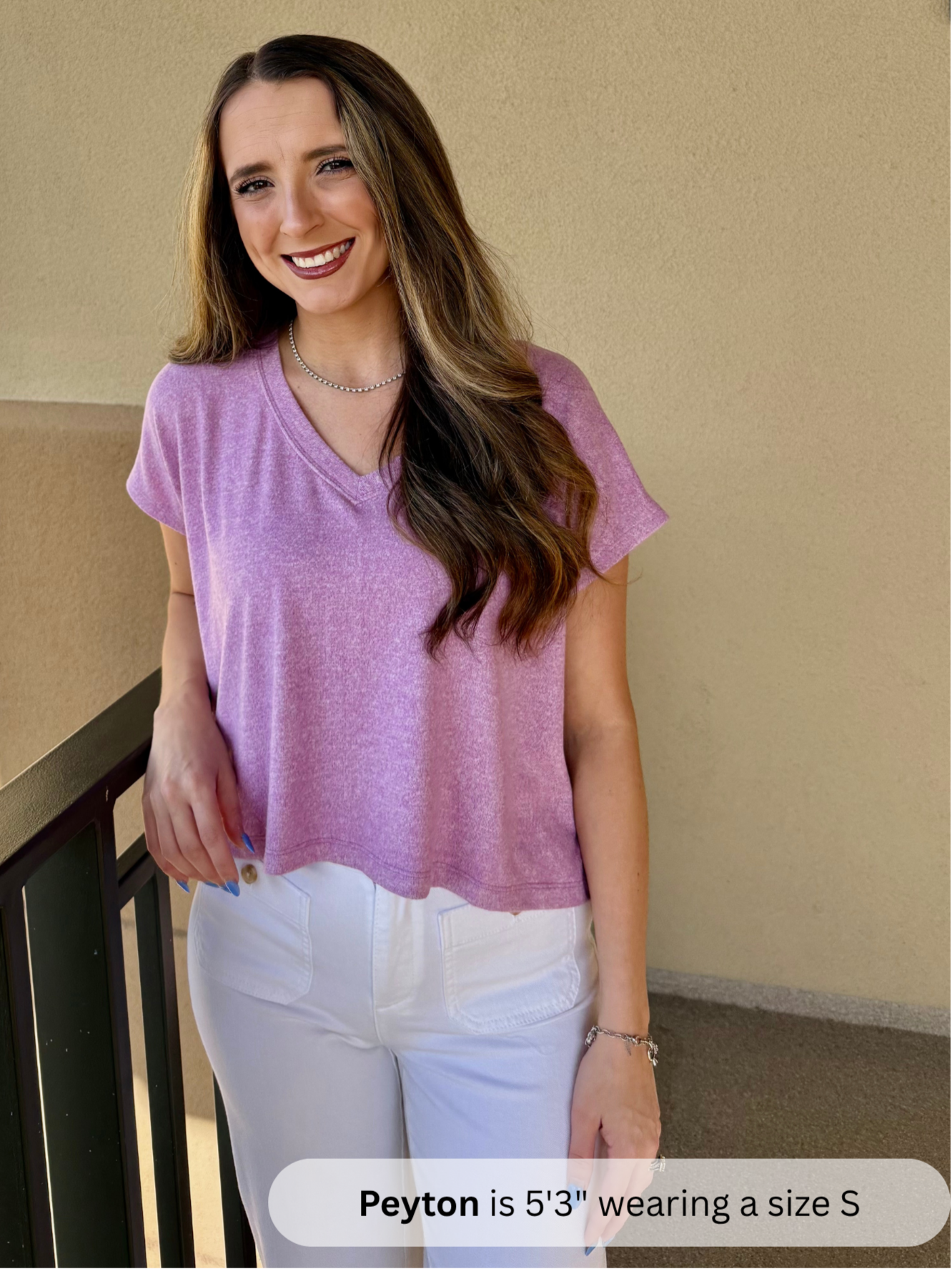 /Mauve/ Woman wearing a purple shirt and white pants standing against a beige wall.