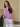 /Mauve/ Woman wearing a purple shirt and white pants standing against a beige wall.