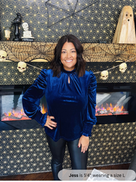 Woman wearing a blue velvet top standing in front of a Halloween-themed fireplace.