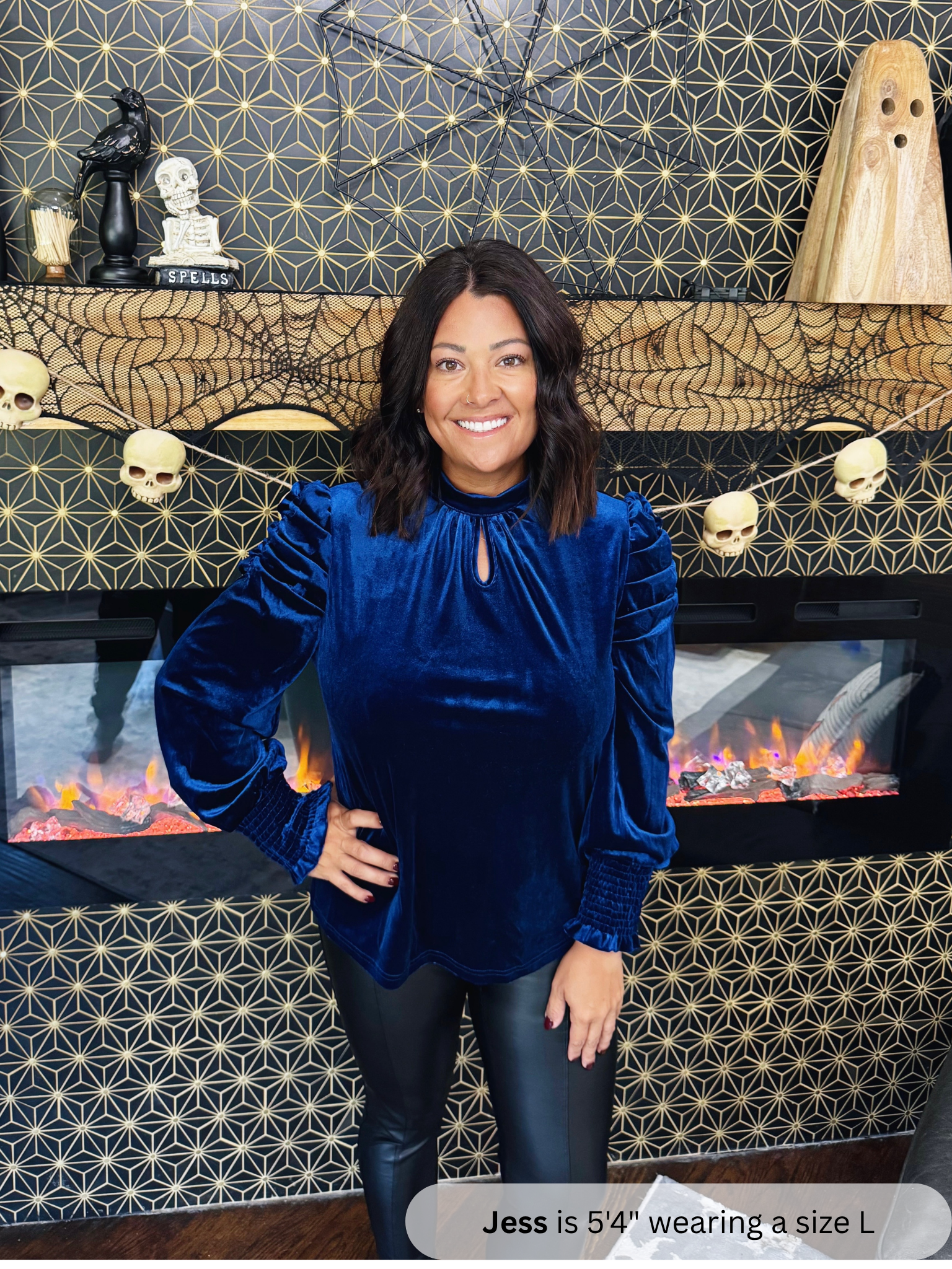 Woman wearing a blue velvet top standing in front of a Halloween-themed fireplace.