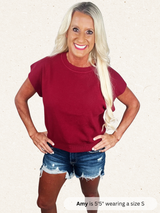 Woman wearing a maroon t-shirt and denim shorts on a white background