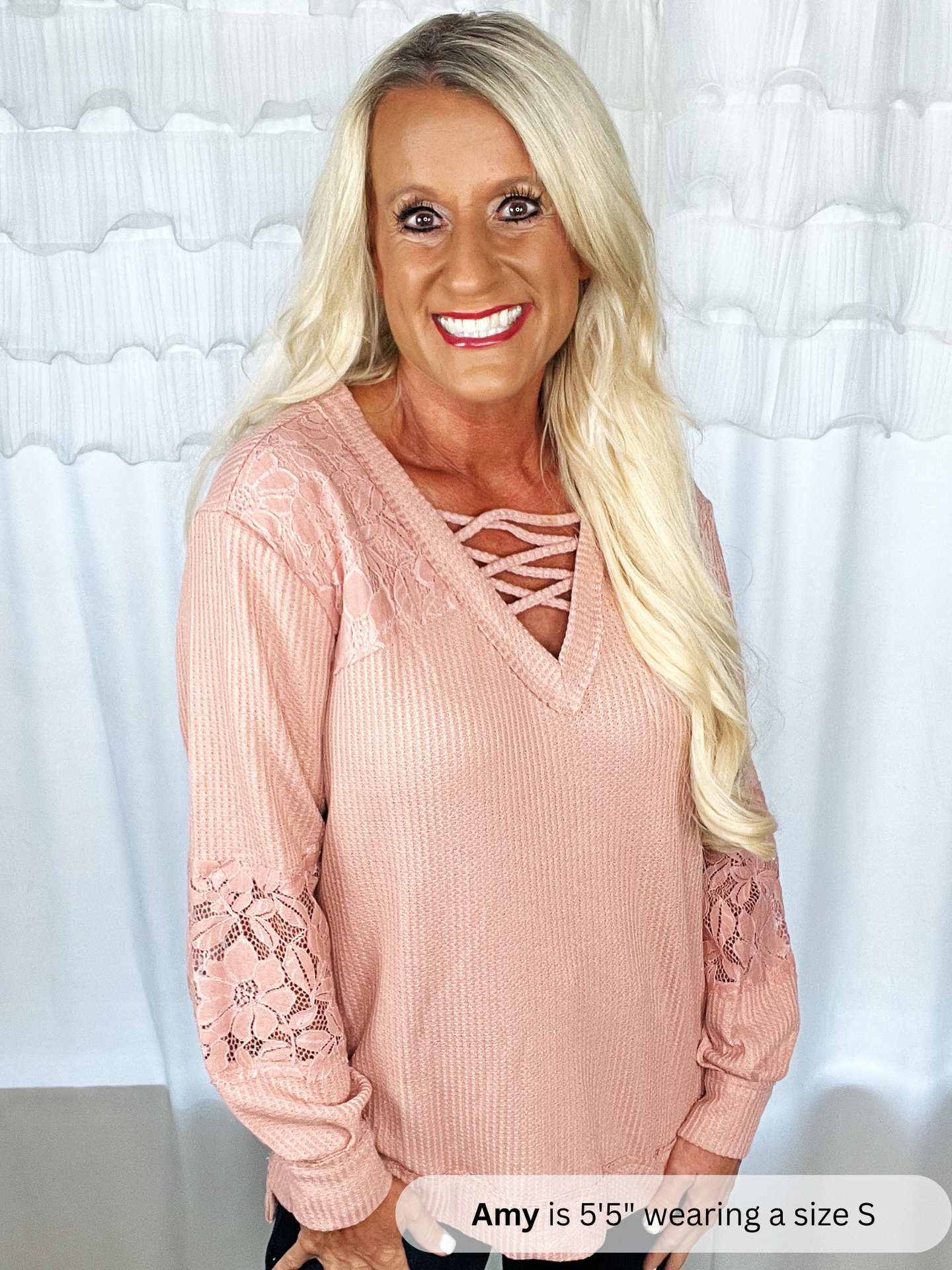Woman wearing a pink sweater with lace details against a white curtain background