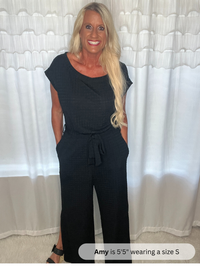 Woman wearing a black jumpsuit standing in front of white curtains