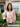 Woman wearing a floral blouse standing outside a house with flowers and a door decoration.