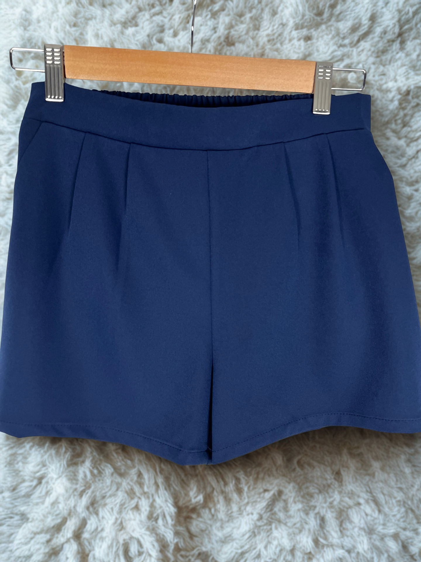 Navy blue skirt on a wooden hanger against a textured white background
