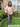 Woman standing outdoors in a garden wearing a floral blouse and gray pants.