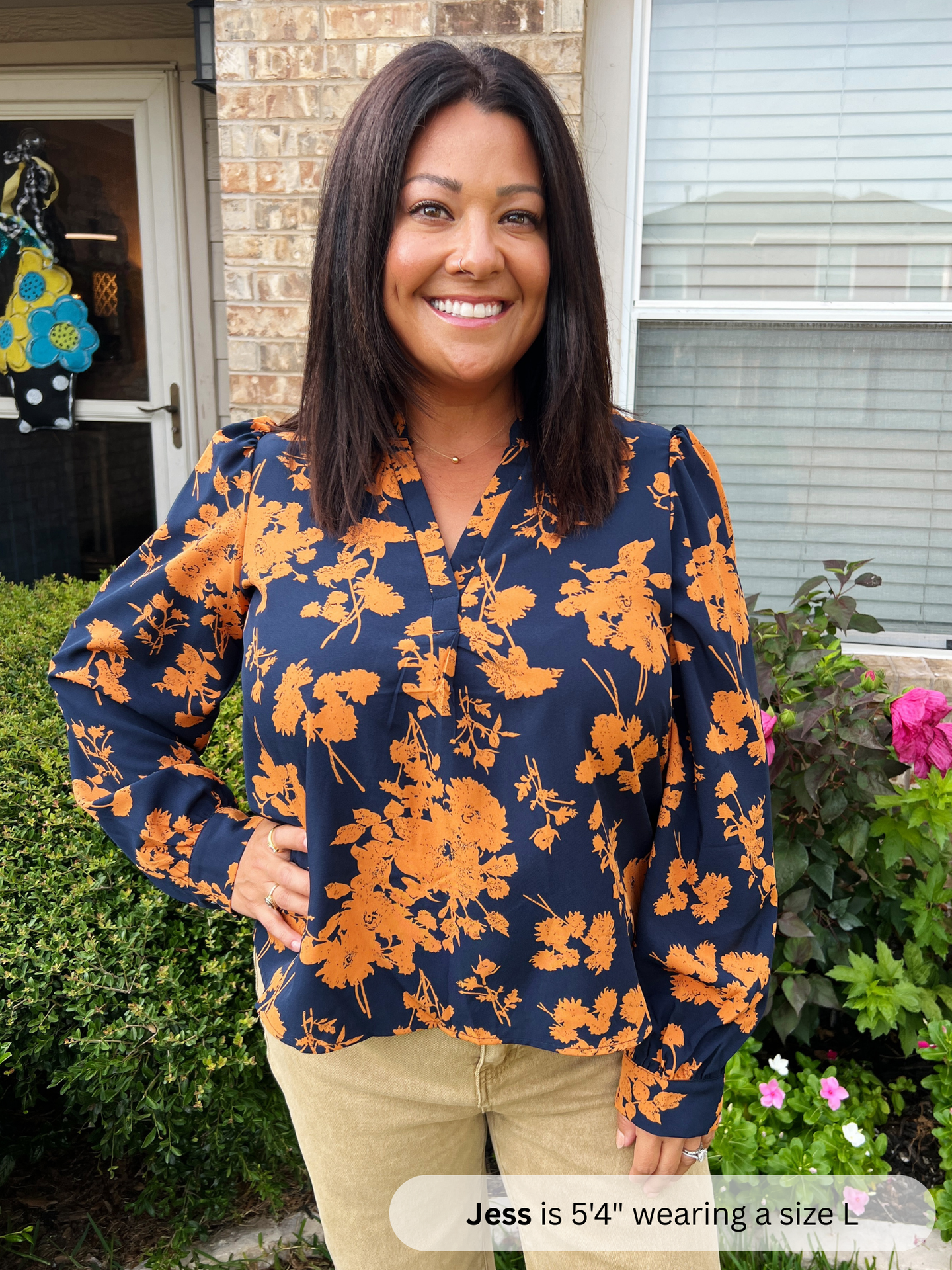 Woman wearing a navy blue floral blouse with orange flowers standing outside a house.