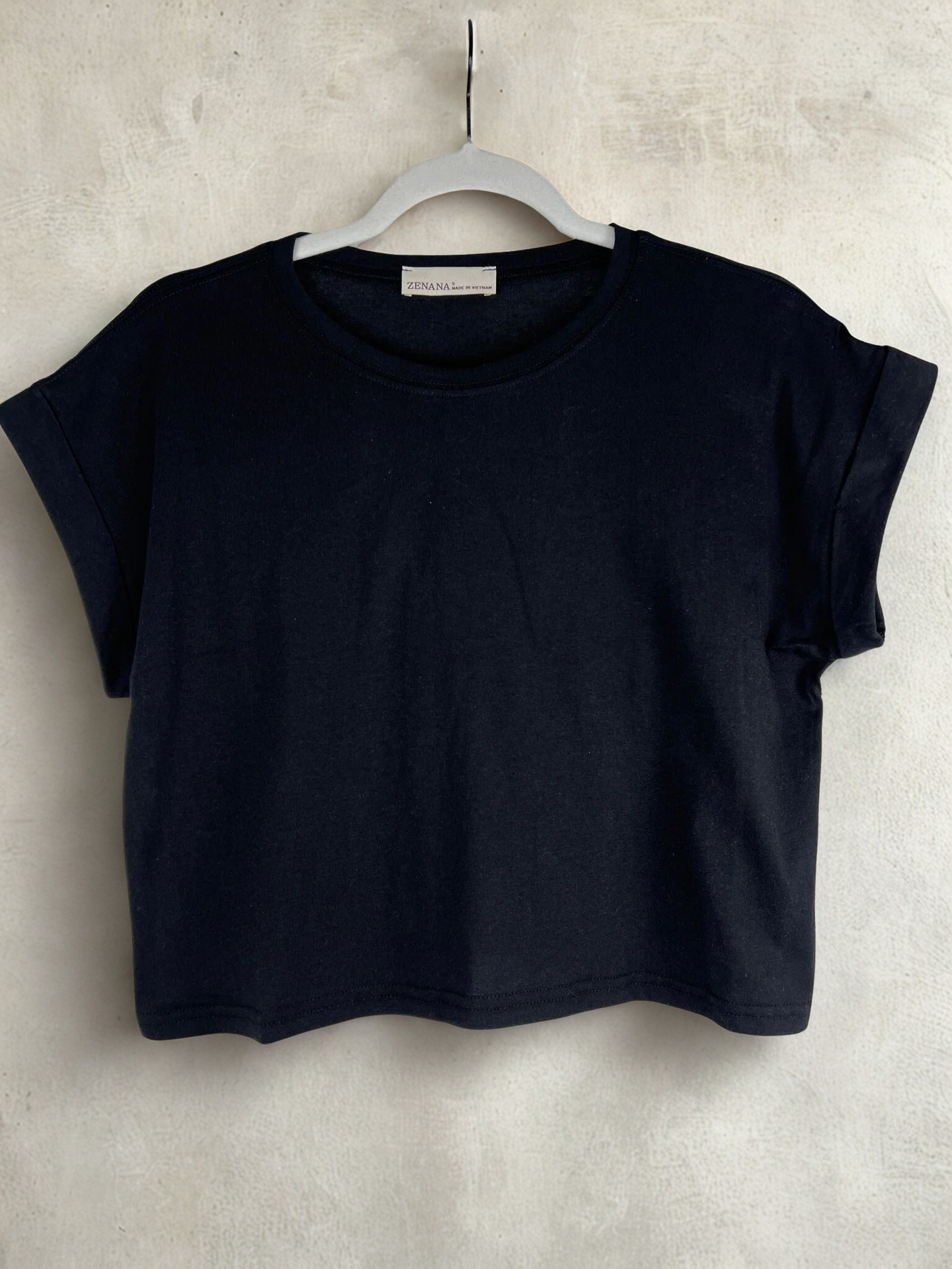 /Black/ Black t-shirt on a hanger against a light gray background