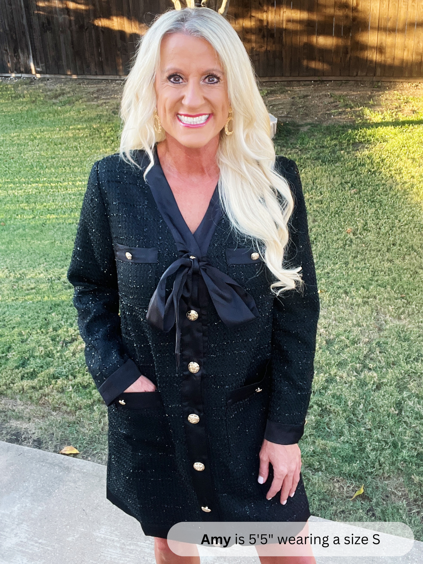 Woman wearing a black dress with gold buttons outdoors on a grassy area.