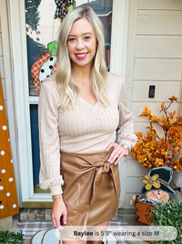 Woman wearing a beige top and brown skirt standing in front of a house with autumn decorations.