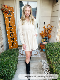 Woman in a white dress standing on a porch with fall decorations.