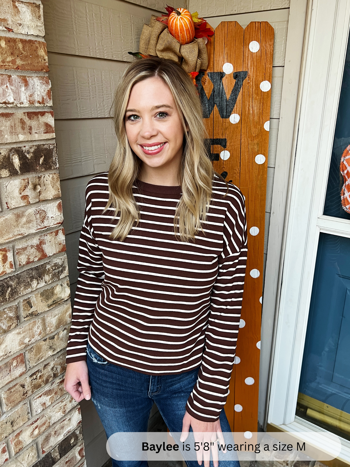 Woman wearing a striped shirt standing in front of a decorated door with pumpkins.