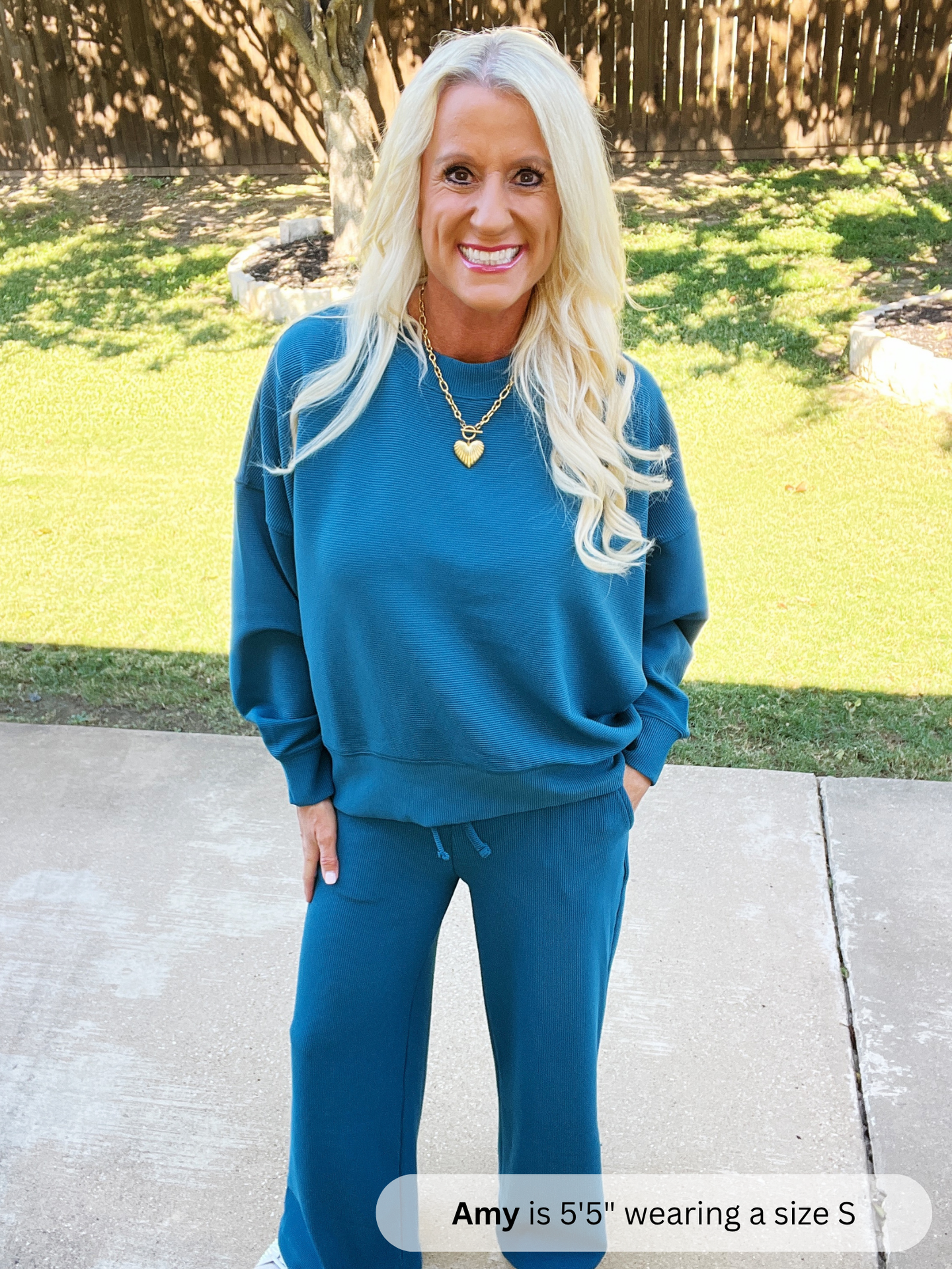 Woman wearing a blue sweatshirt and pants standing outdoors on a sunny day.