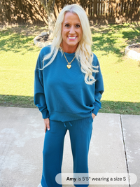 Woman wearing a blue sweatshirt and pants standing outdoors on a sunny day.