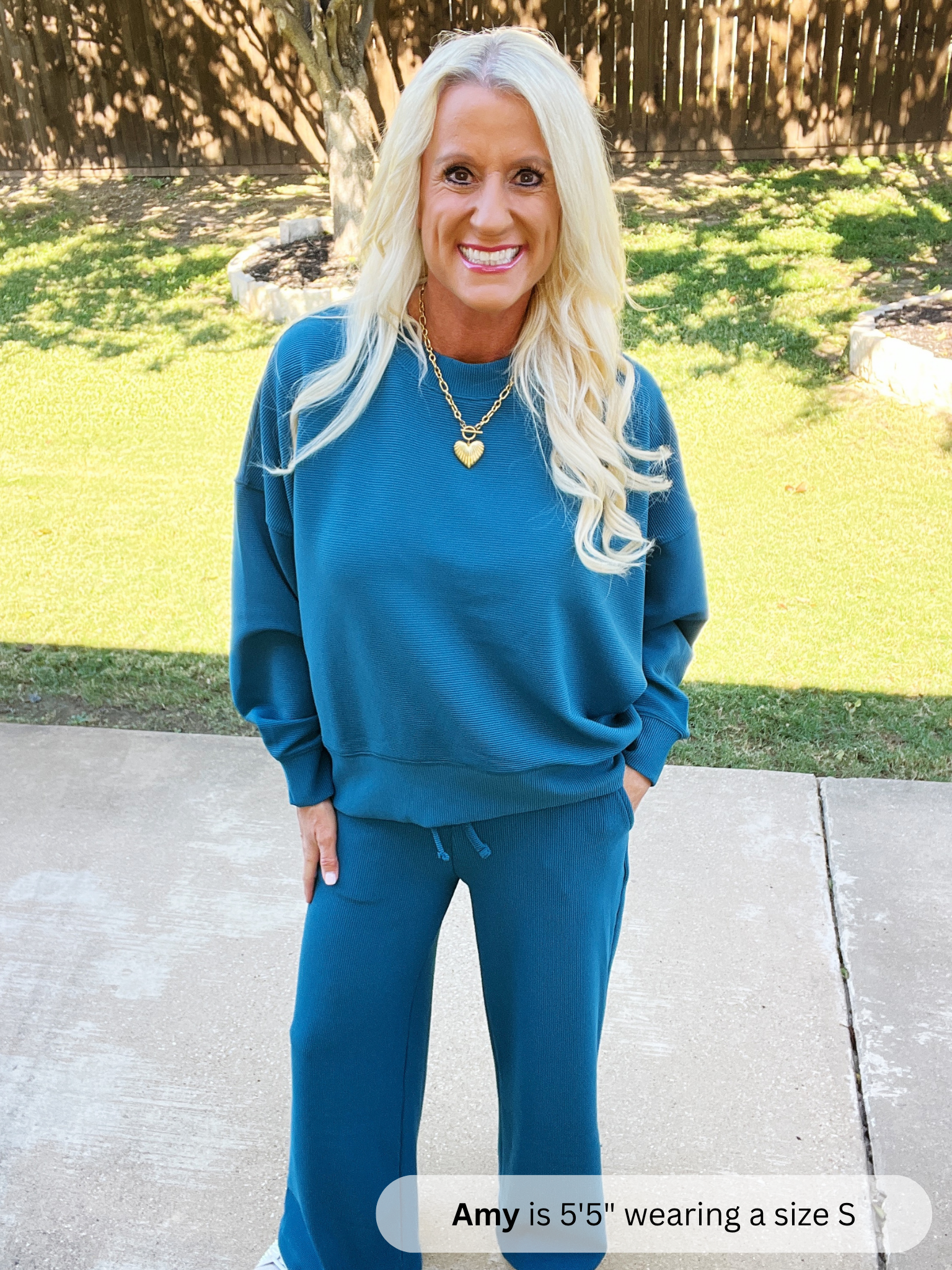 Woman wearing a blue sweatshirt and pants standing outdoors on a sunny day.