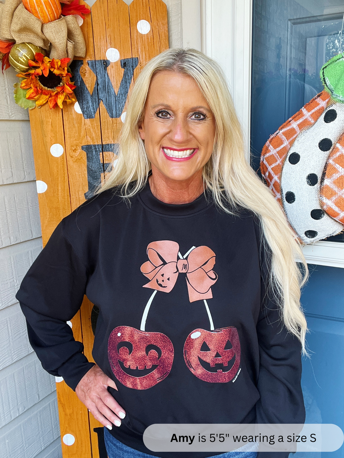Woman wearing a black sweatshirt with Halloween-themed design in front of a decorated door.