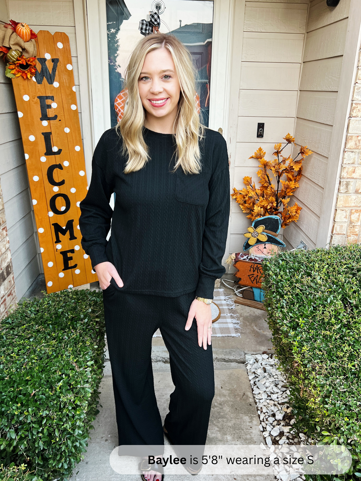 Woman in a black outfit standing in front of a house with Halloween decorations.