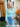 Woman in a light blue sweater and jeans standing in front of a 'Welcome' sign with autumn decorations.