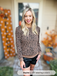 Woman wearing a leopard print sweater and black shorts in an outdoor setting with Halloween decorations.