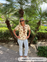 Woman wearing a patterned shirt and white pants standing in front of palm trees.
