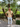 Woman wearing a patterned shirt and white pants standing in front of palm trees.