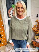Woman wearing a green sweater and blue jeans standing in front of a decorated door with fall decorations.
