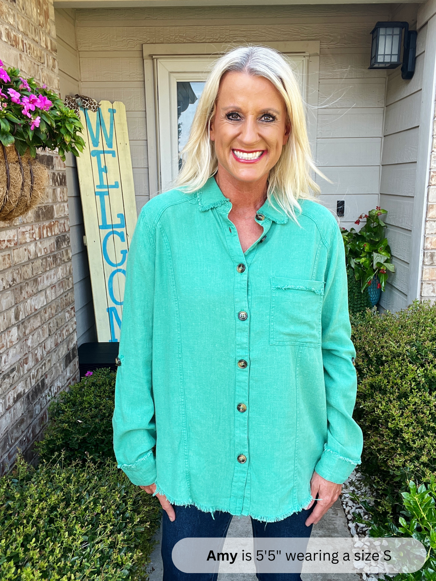 Woman wearing a teal shirt standing outside a house with a 'Welcome' sign.