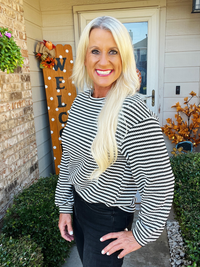 Woman in a striped shirt standing in front of a house with decorative 'Welcome' sign.