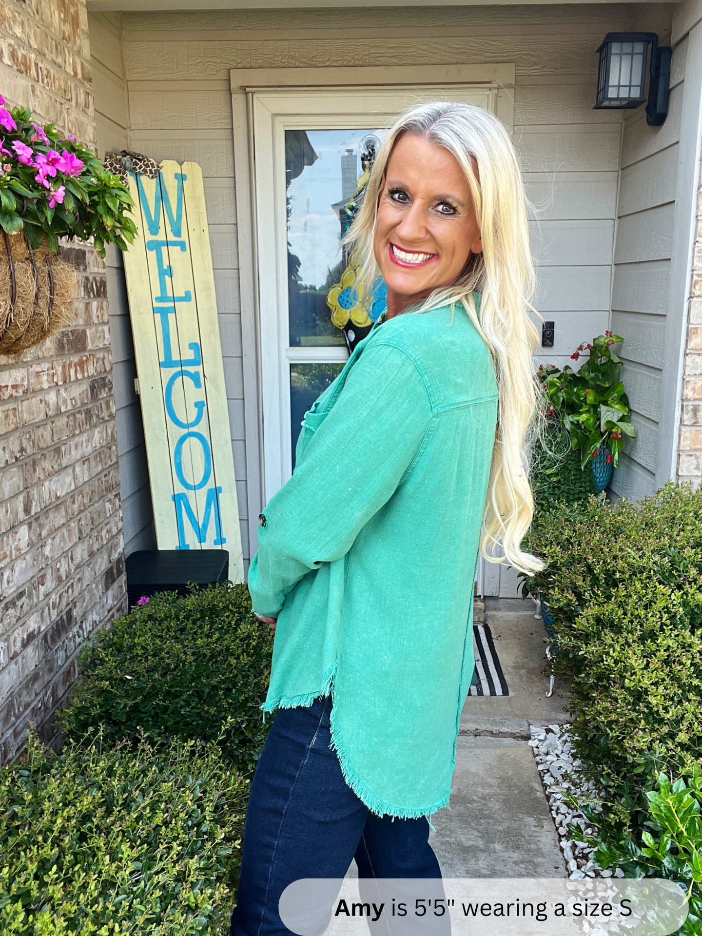 Woman in a teal sweater standing in front of a house with a 'WELCOME' sign.