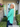 Woman in a teal sweater standing in front of a house with a 'WELCOME' sign.