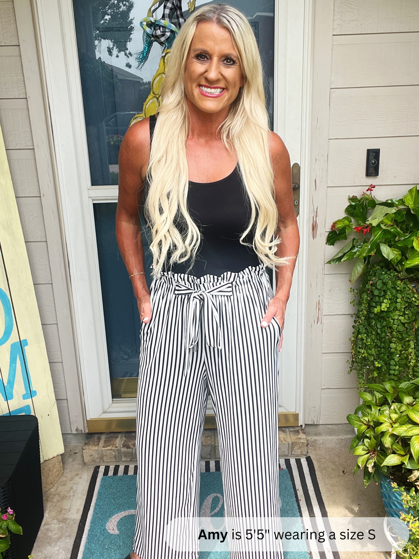 Woman wearing a black tank top and striped pants standing outside a house.
