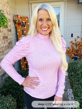 Woman wearing a pink sweater standing outside a house with decorative elements.