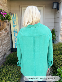 Person wearing a teal jacket standing in front of a house with a 'Welcome' sign.