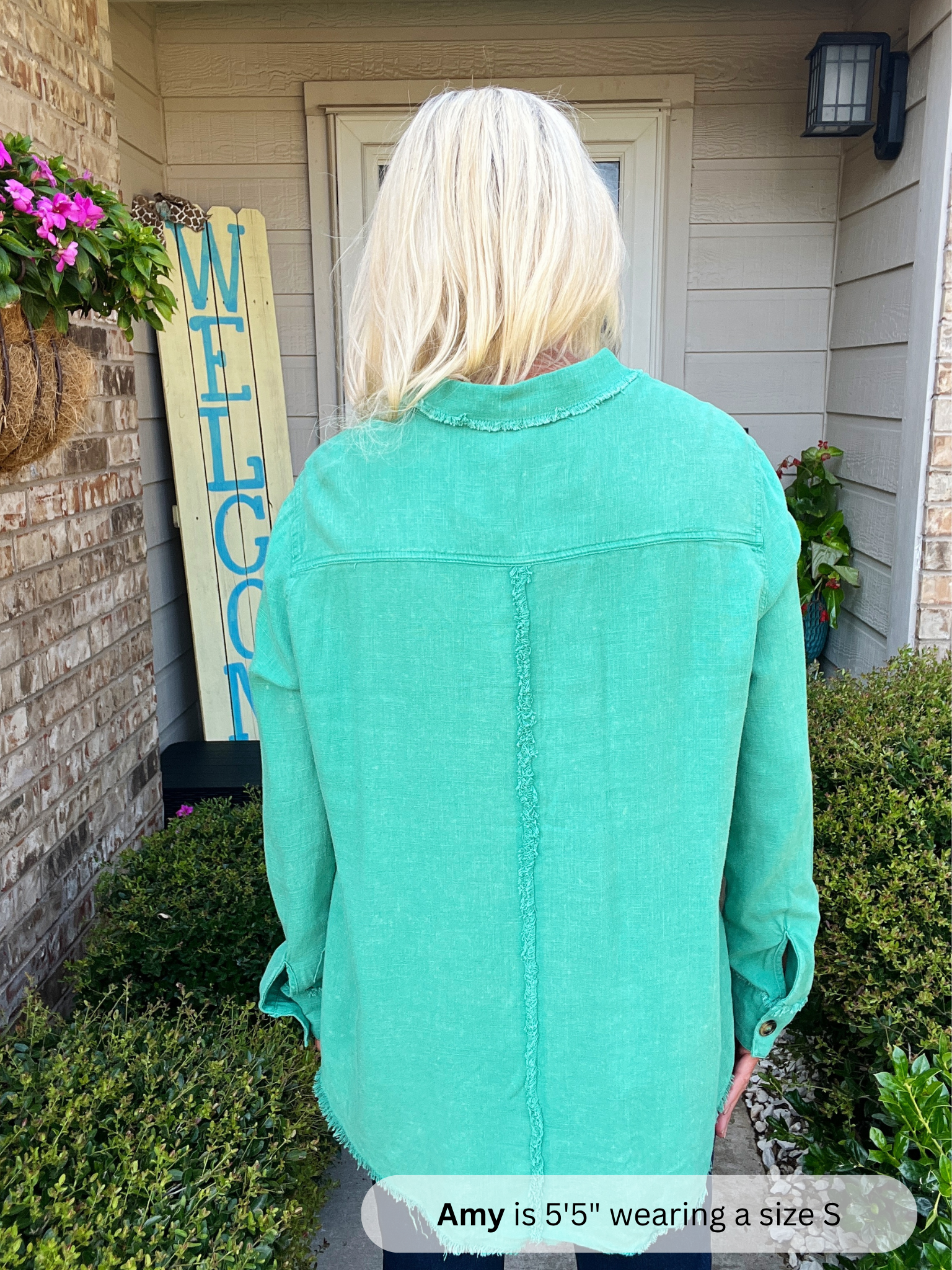 Person wearing a teal jacket standing in front of a house with a 'Welcome' sign.