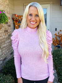 Woman wearing a light purple turtleneck sweater standing outside a house.